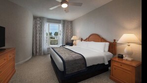 Une chambre d’hôtel comprenant un lit, deux lampes de chevet, un ventilateur de plafond, une télévision, une commode en bois et une fenêtre avec des rideaux.
