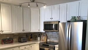 A modern kitchen with white cabinets, stainless steel appliances, and a tiled backsplash. - Seaside Villas II, Oceanfront Condo (Folly Beach)