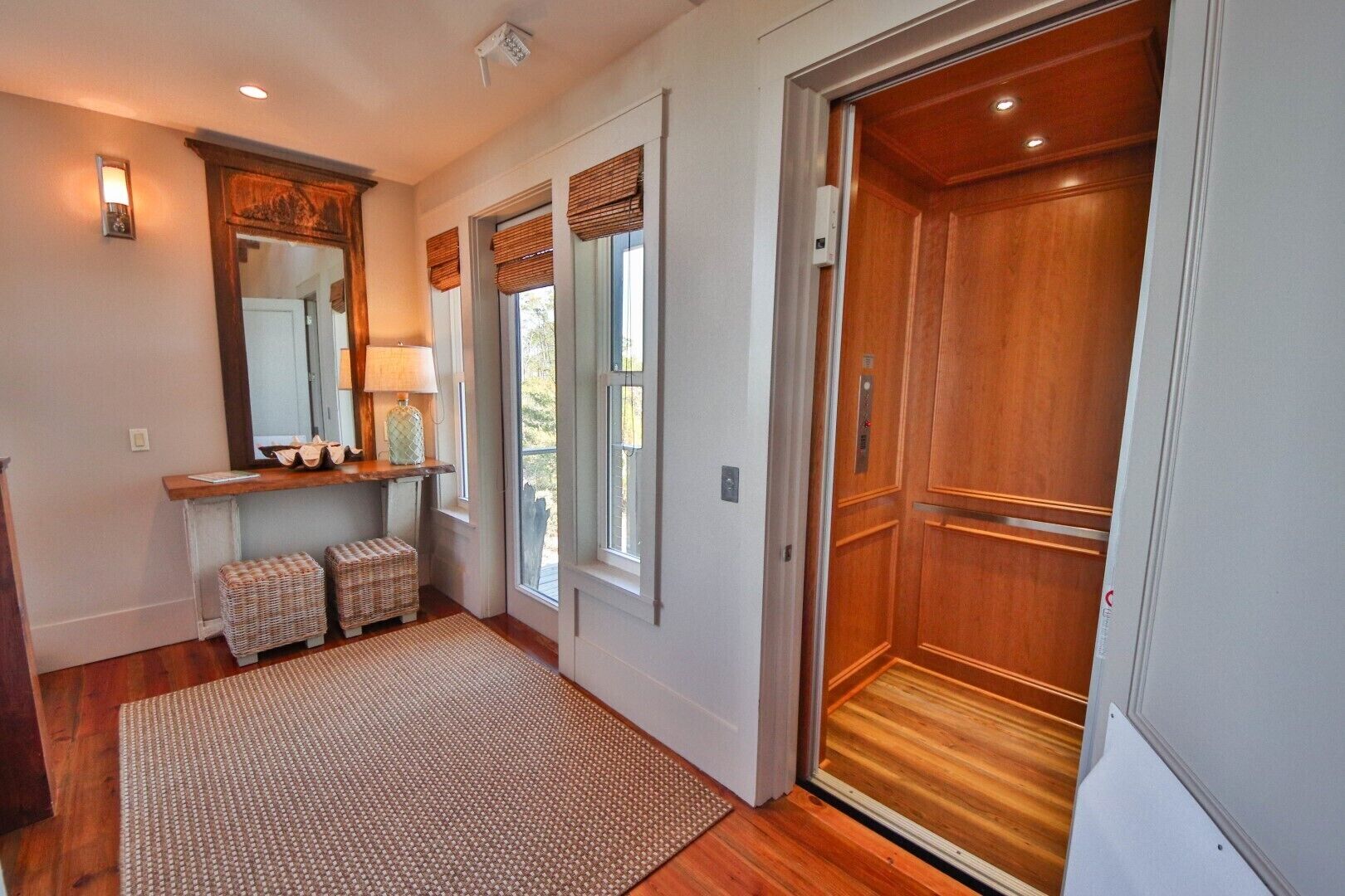 A hallway with a wooden floor, a mirror, a lamp, wicker baskets, and a wooden door.