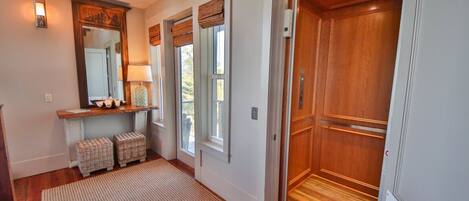 A hallway with a wooden floor, a mirror, a lamp, wicker baskets, and a wooden door.