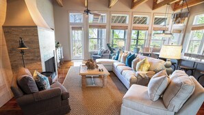 A spacious living room with a fireplace, large windows, and a high ceiling. - 'Forcynthia' Luxury Bay Home 4BR/4.5BA ,w/ dock, kayak launch (St. George Island)