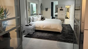Une chambre moderne avec un grand lit, des tables de chevet, un miroir et une vue sur le couloir.