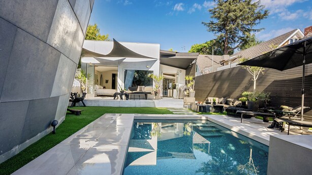 Un espace piscine extérieur moderne, doté d’un design géométrique, entouré d’une terrasse aménagée avec des sièges et des plantes en pot.