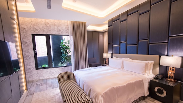 Un dormitorio moderno con una cama grande, un banco, un televisor y una ventana con cortinas.