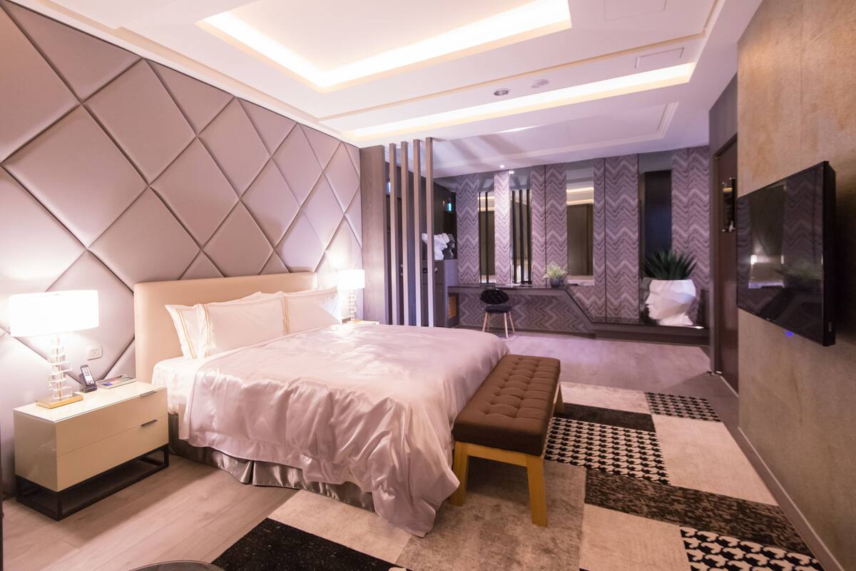 Ein modernes Hotelzimmer mit einem großen Bett, Nachttischen, einer Bank und einem Fernseher.