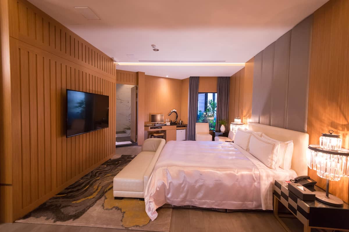 Ein modernes Hotelzimmer mit einem großen Bett, einem Schreibtisch, einem Fernseher und einem durch eine offene Tür einsehbaren Badezimmer.