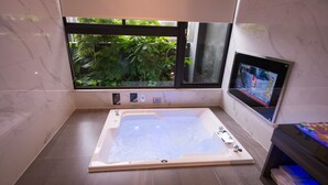 Un baño moderno con una bañera grande, una ventana con vistas a la vegetación y un televisor montado.