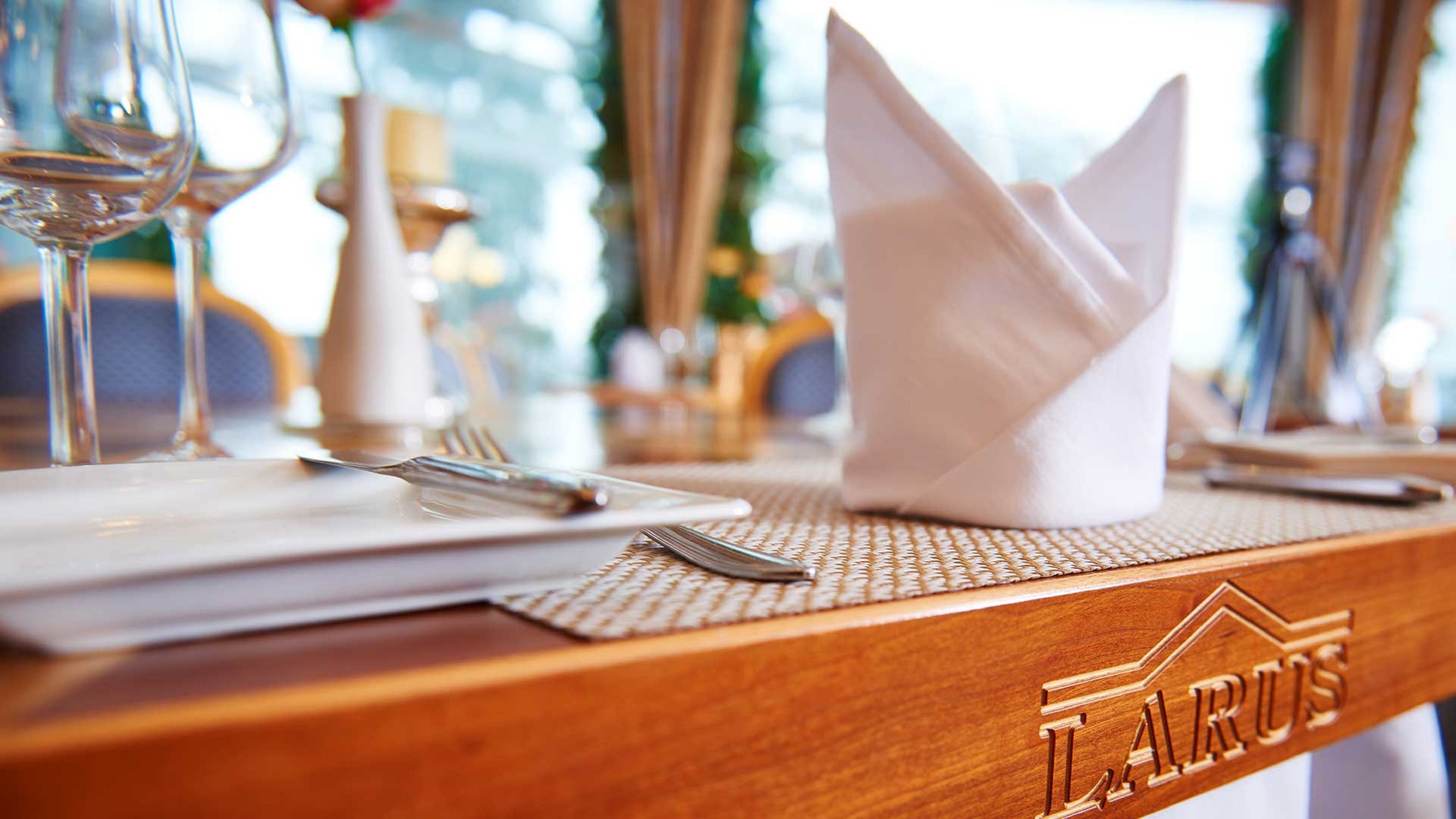 Una mesa de comedor dispuesta con esmero, con servilleta, tenedor y copa de vino, y una encimera de madera con el nombre 'TARUS' grabado.