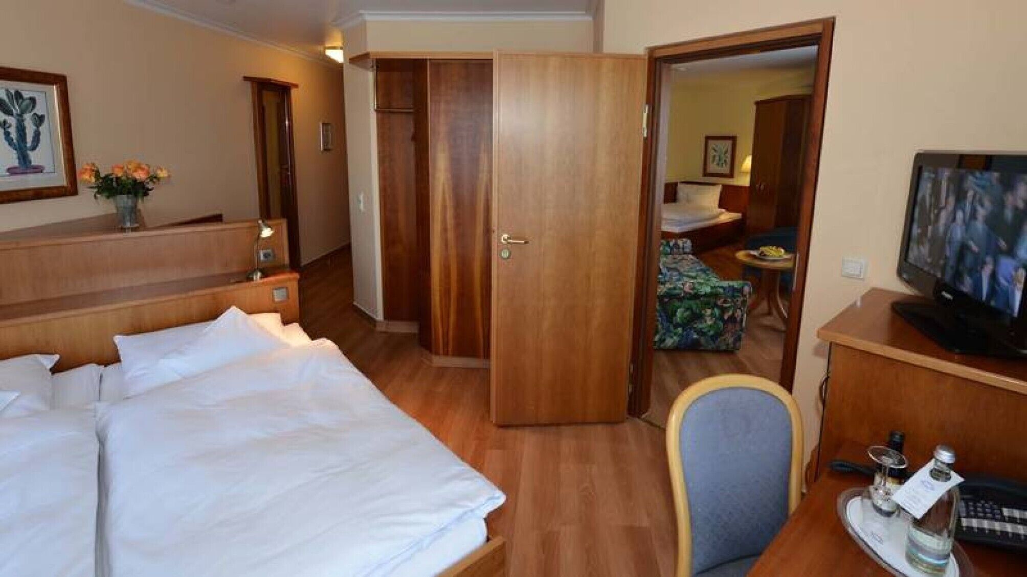 A hotel room with a bed, a desk with a computer, a TV, and a bathroom visible through an open door.