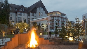 A courtyard with a fire feature, surrounded by buildings with balconies and a covered seating area. - Rheinhotel LARUS (Kaltenengers)