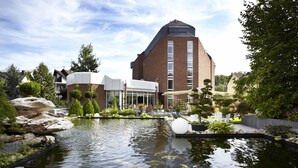 A modern building with a pond and surrounding greenery. - Rheinhotel LARUS (Kaltenengers)