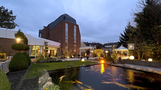 A courtyard with a koi pond, brick buildings, and a gazebo. - Rheinhotel LARUS (Kaltenengers)