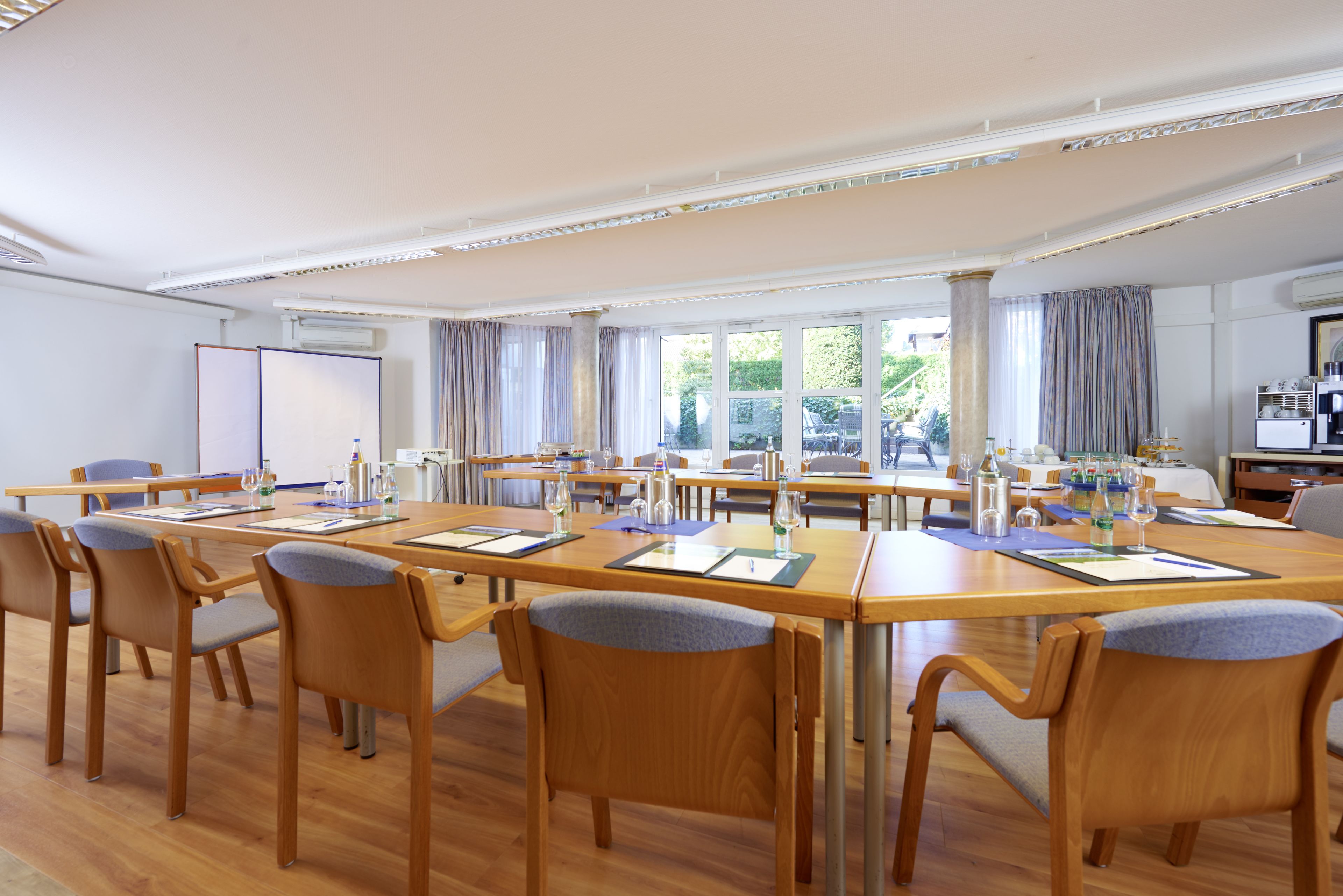 A conference room with wooden tables and chairs, large windows, and an air conditioning unit.