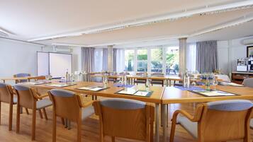 A conference room with wooden tables and chairs, large windows, and an air conditioning unit.