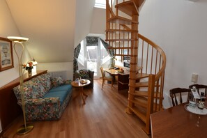 A cozy room with a wooden staircase, a sofa, a dining table, and a small round table with a lamp.