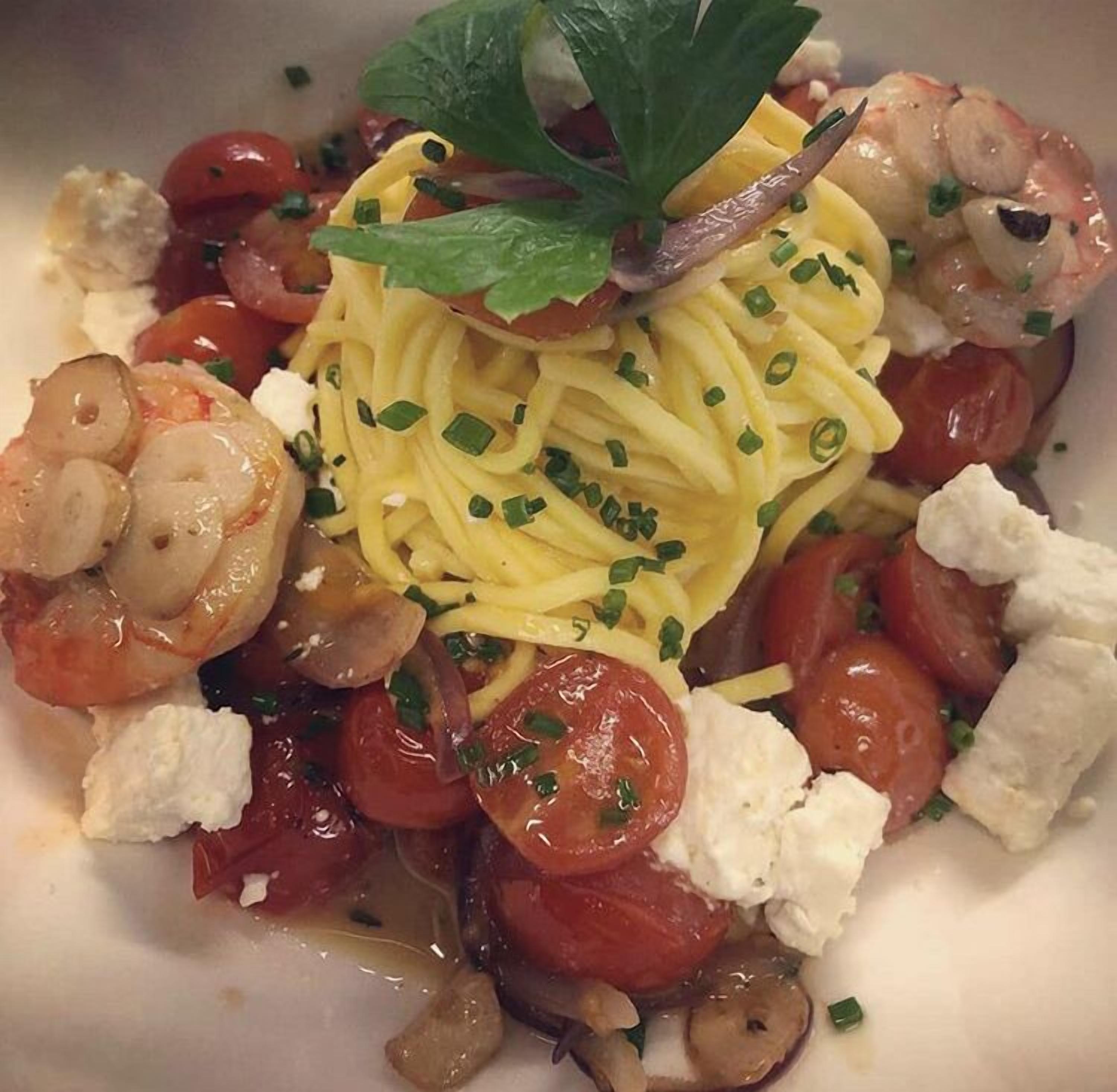 A plate of pasta with shrimp, cherry tomatoes, and cheese.