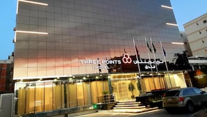 Un hotel moderno con fachada de vidrio, un cartel llamativo que dice "THREE POINTS HOTEL" y una escalera que conduce a la entrada.