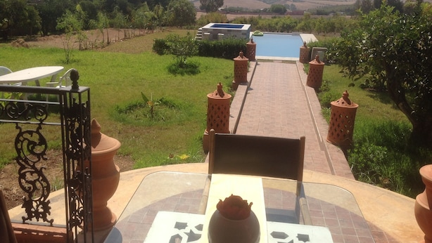 A patio with a table and chairs, a view of a swimming pool, and a garden with a pathway. - Hotel Le Palais d hotes (Salé)