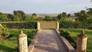 A paved pathway leading to a gate with decorative pillars, surrounded by lush greenery and a view of distant fields. - Hotel Le Palais d hotes (Salé)