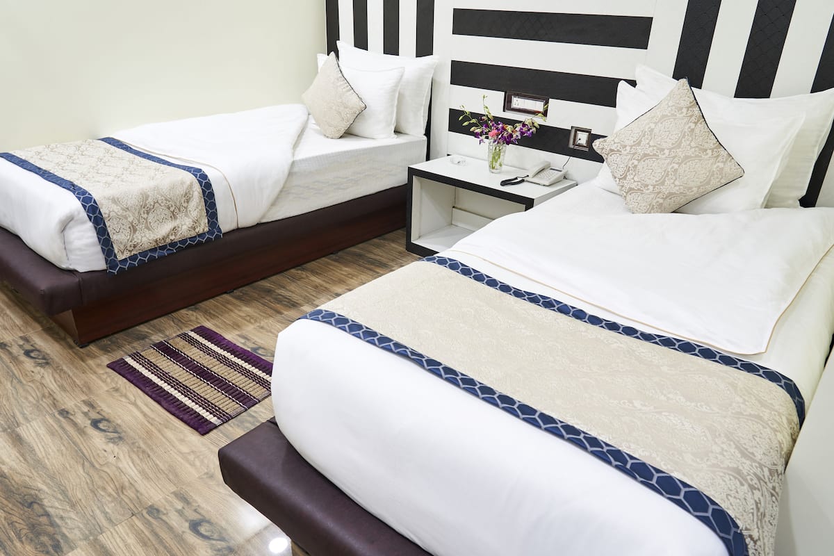 Una habitación de hotel con dos camas, una mesita de noche y otra con un jarrón de flores.