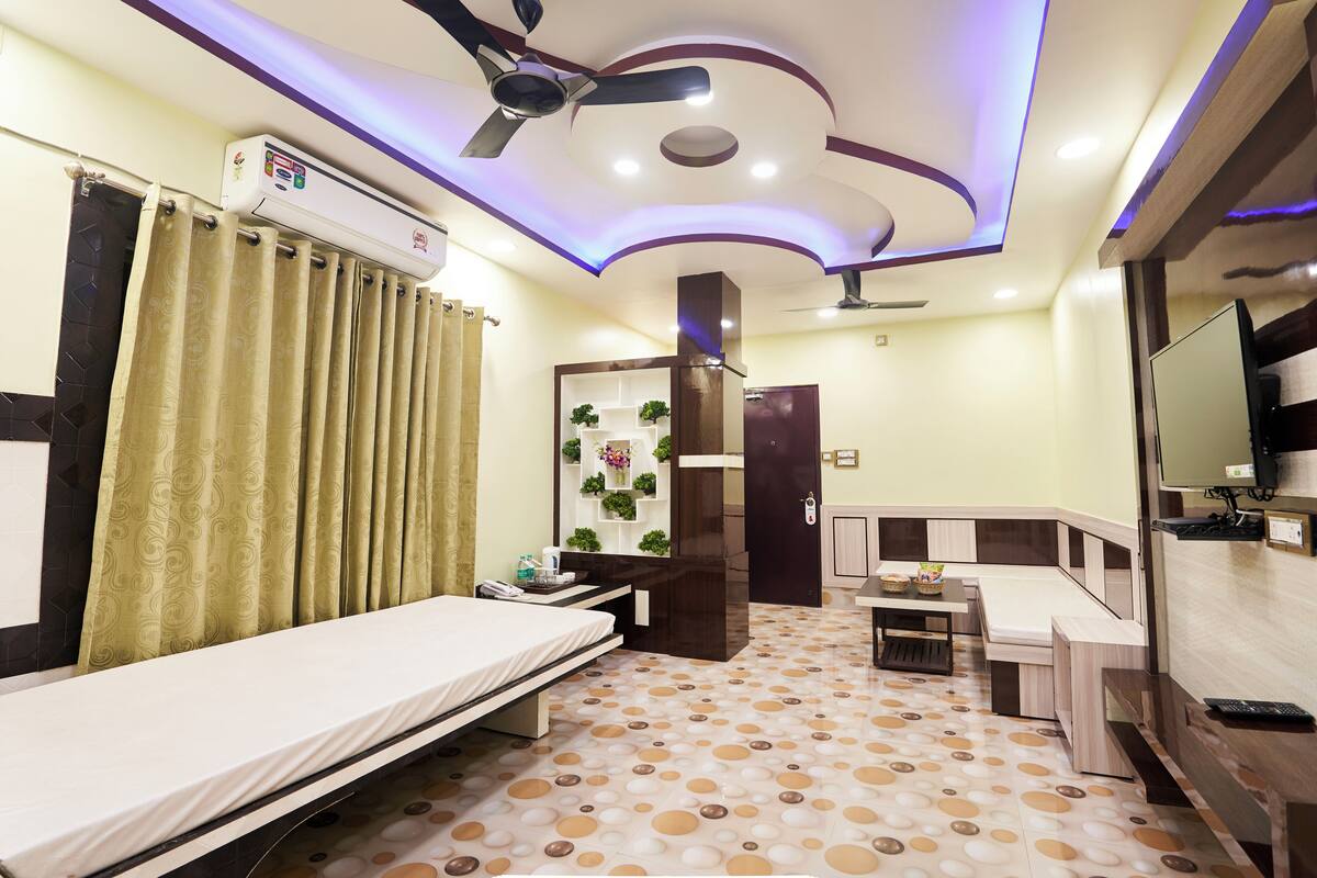 Habitación de hotel con cama, escritorio, silla, televisor y ventilador de techo.