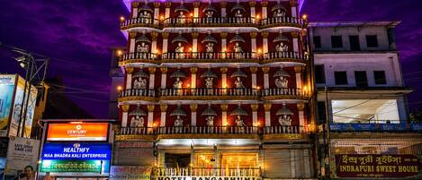 Un immeuble à plusieurs étages doté de balcons, une enseigne indiquant « Hôtel Bangabhumi », et diverses devantures de magasins.
