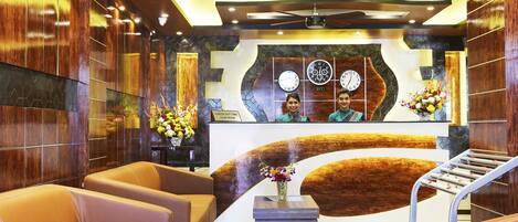 A hotel lobby with a reception desk, two sofas, a clock, and a decorative wall.