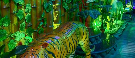 A vibrant indoor garden with a large tiger statue, bamboo structures, and various plants.