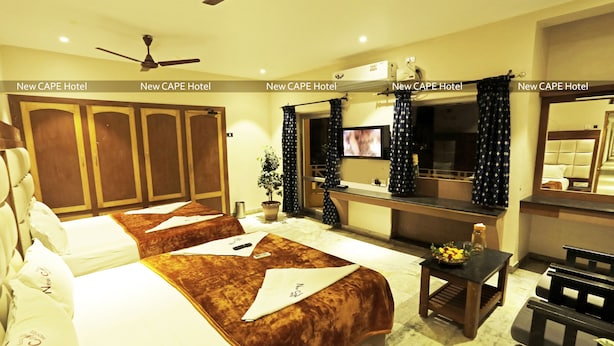A hotel room with two beds, a TV, a desk, and a ceiling fan. - New Cape Hotel (Nagercoil)