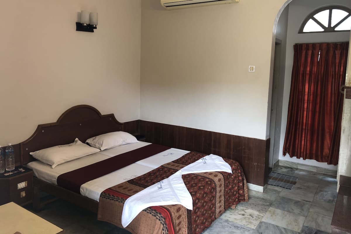 Cama bem arrumada com colcha estampada, mesa de cabeceira com garrafa de água e aparelho de ar condicionado acima da cama.