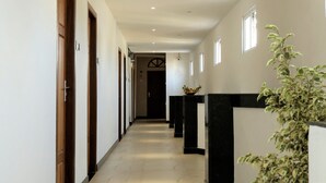 A hallway with wooden doors, a black and white counter, and a plant. - New Cape Hotel (Nagercoil)