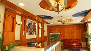 A reception area with a wooden reception desk, a red sofa, a fish tank, and a chandelier. - New Cape Hotel (Nagercoil)