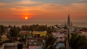 A coastal cityscape at sunset with a prominent church and colorful buildings. - New Cape Hotel (Nagercoil)