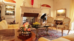 A grand room with a piano, ornate chairs, a fireplace, and a large table with a vase of flowers. - Relais Tenuta del Gallo (Amelia)