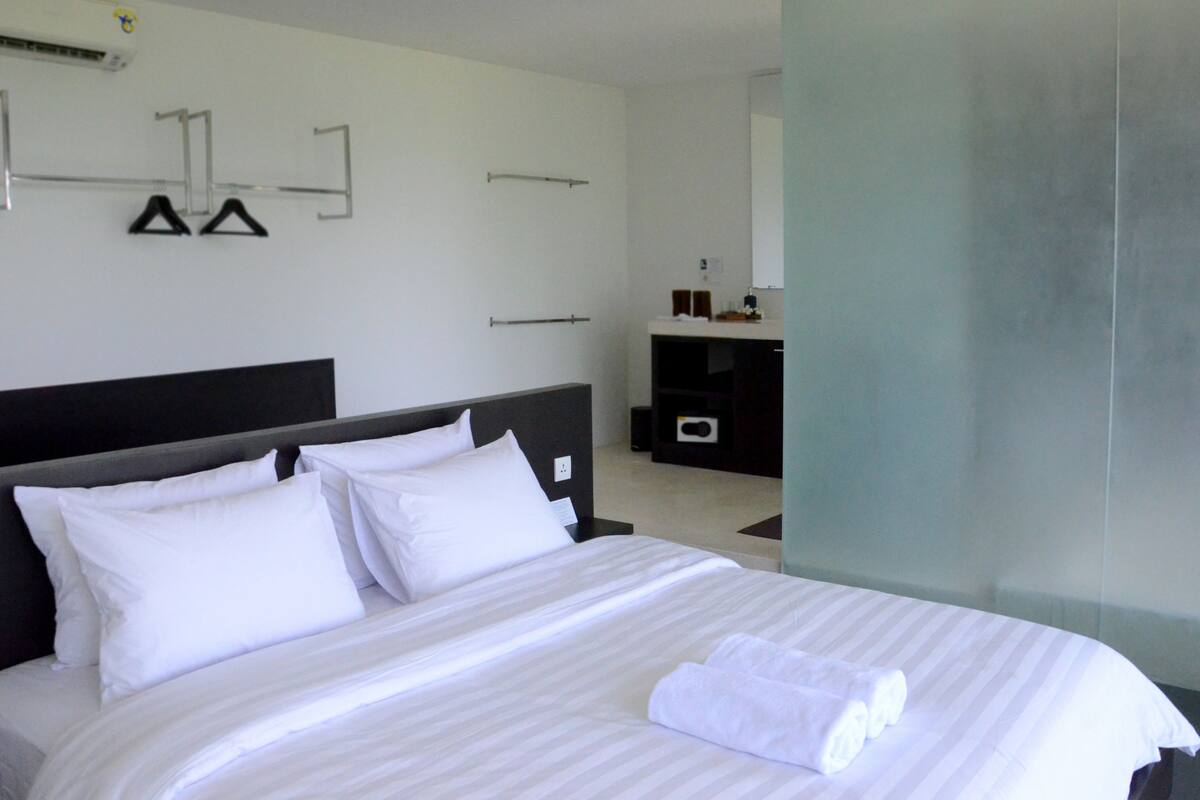 A modern hotel room with a large bed, a dark headboard, and a minimalist design.