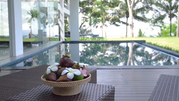 Área de piscina tranquila con un cuenco de mimbre que contiene frutas y flores sobre un tapete tejido.