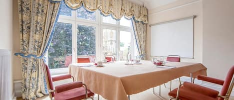 Comedor con una mesa dispuesta para cuatro personas, sillas rojas y vistas a un jardín a través de una ventana con cortinas estampadas.