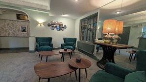 A hotel lobby with two green armchairs, a wooden coffee table, a lamp, and a wall-mounted mirror. - The Walnut Tree Hotel (Bridgwater)