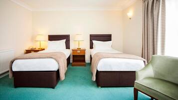 Ein Hotelzimmer mit zwei Betten, einem grünen Sessel und einem kleinen Tisch mit einer Lampe.