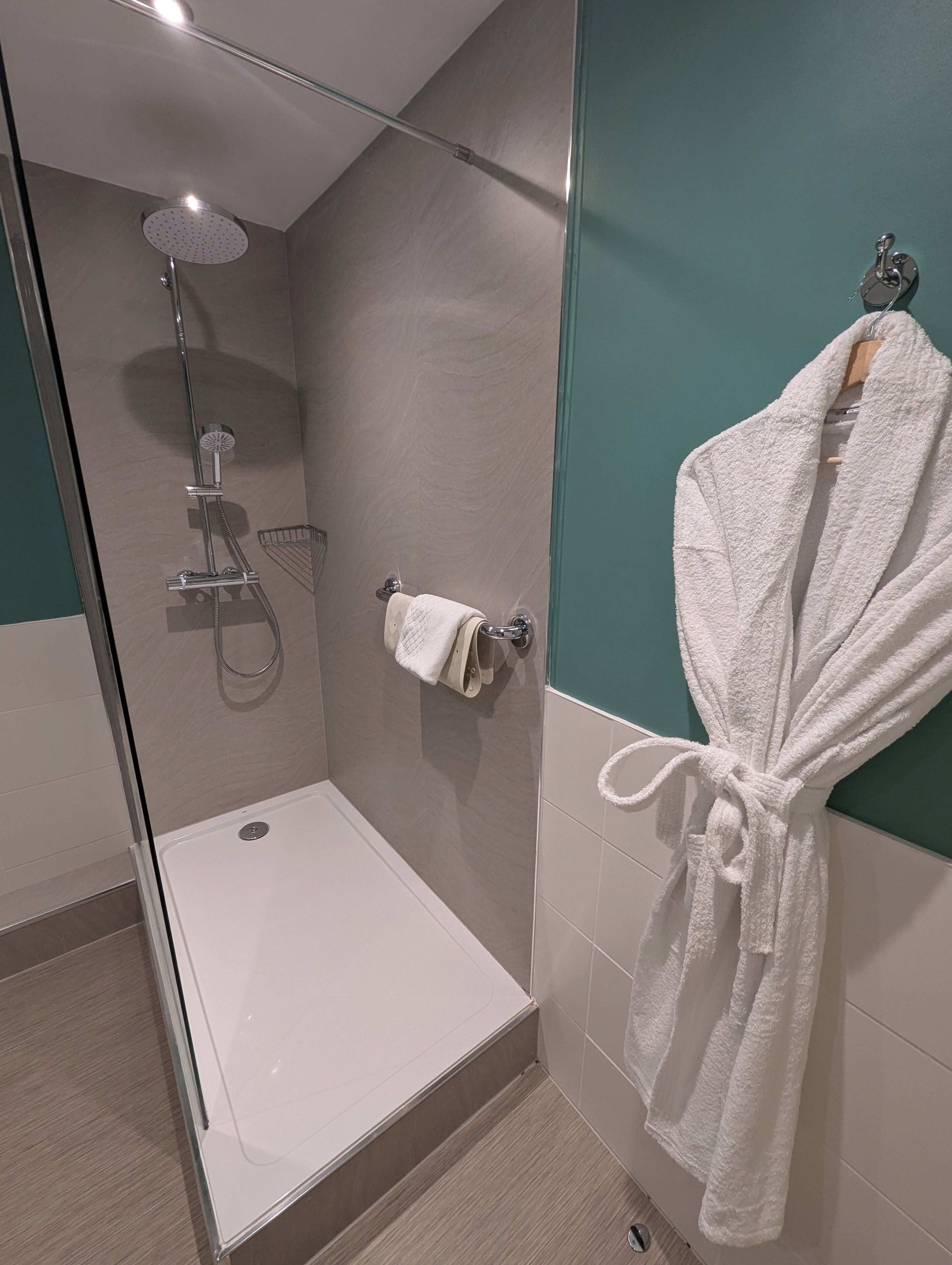 A modern bathroom with a glass-enclosed shower, a white bathtub, and a white robe hanging on the wall.