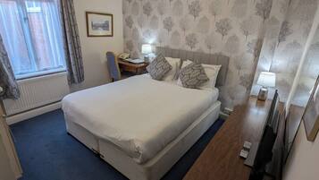 Habitación de hotel con una cama grande, un escritorio con lámpara, una silla, una mesita con bandeja y una ventana con cortinas.