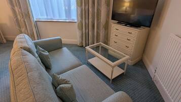 Una sala de estar con sofá, una mesa de centro, televisor y ventana con cortinas.