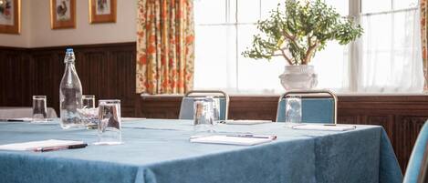 A conference room with a blue tablecloth, glassware, and a potted plant.