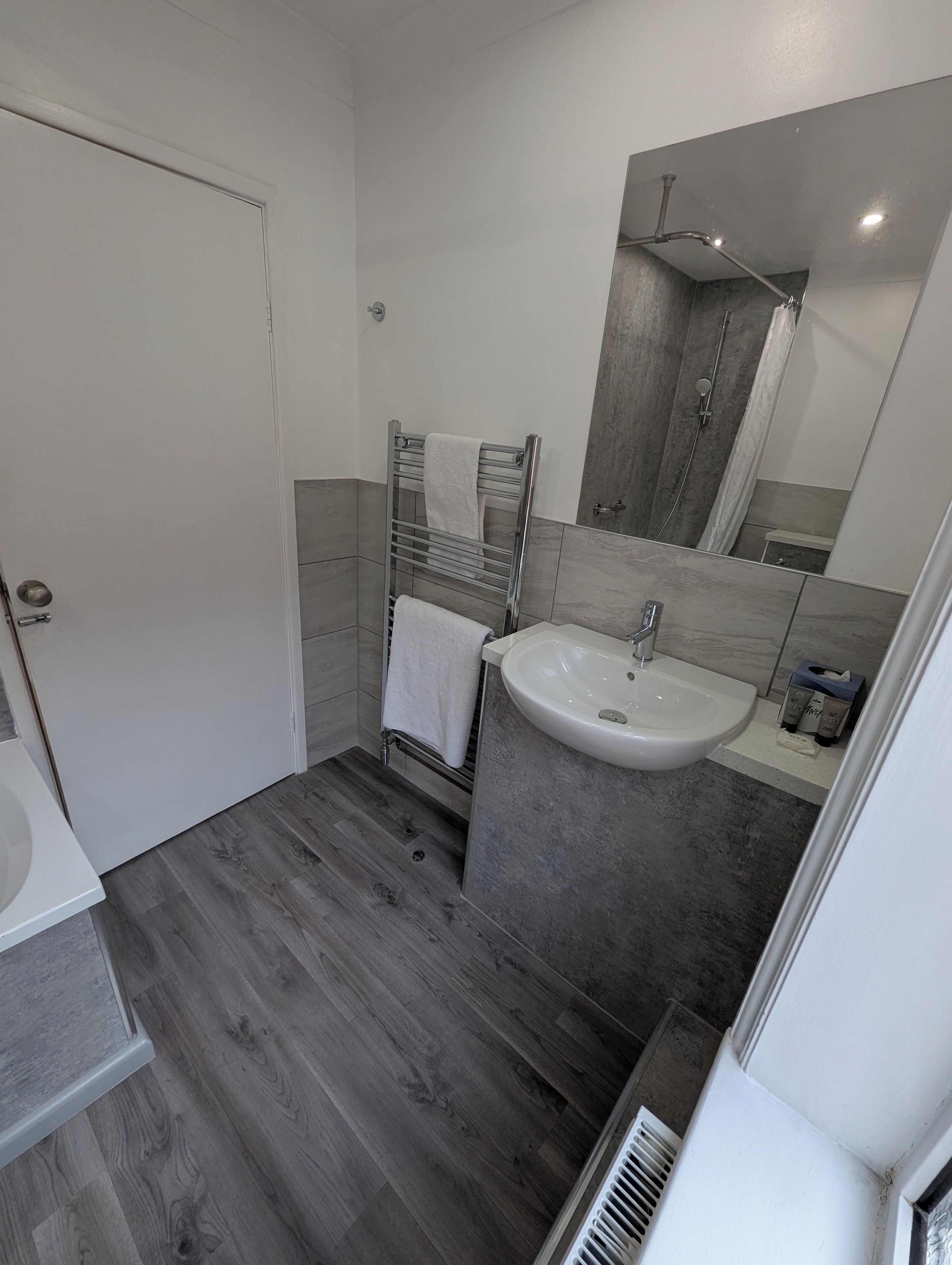 A modern bathroom with a white sink, a glass shower enclosure, and a wooden floor.