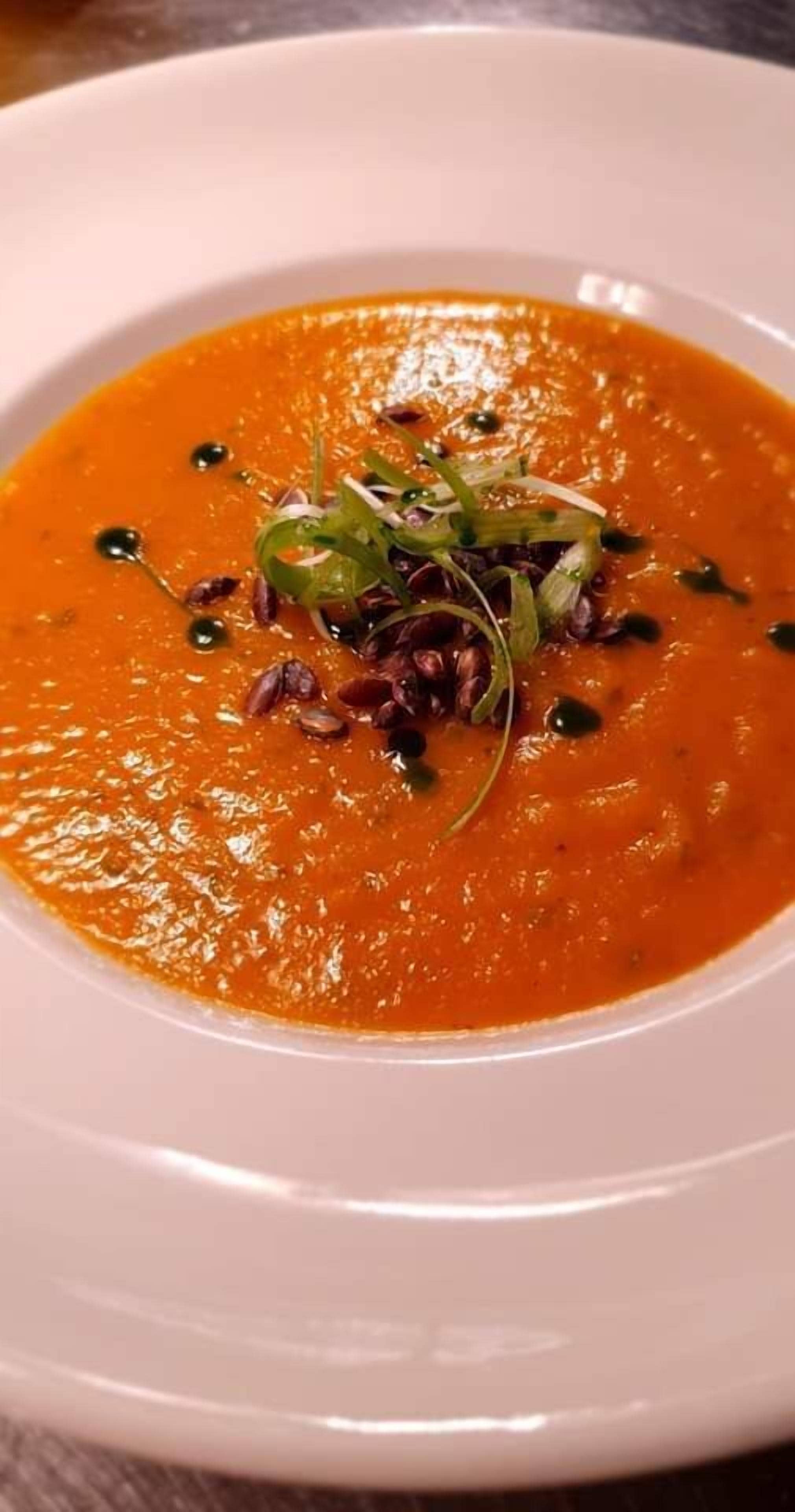 Une assiette blanche contenant un bol de soupe, garni d’herbes et de graines vertes.