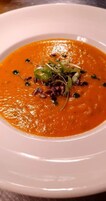 Un plato blanco con un bol de sopa adornado con hierbas verdes y semillas.