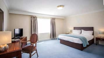 A hotel room with a bed, a desk with a lamp, a chair, a television, and curtains.