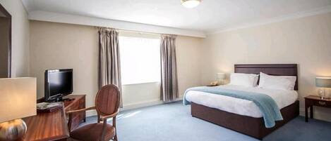A hotel room with a bed, a desk with a lamp, a chair, a television, and curtains.