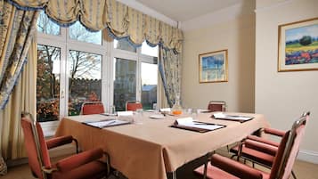 A conference room with a table set for a meeting, chairs, a window with curtains, and a painting on the wall.