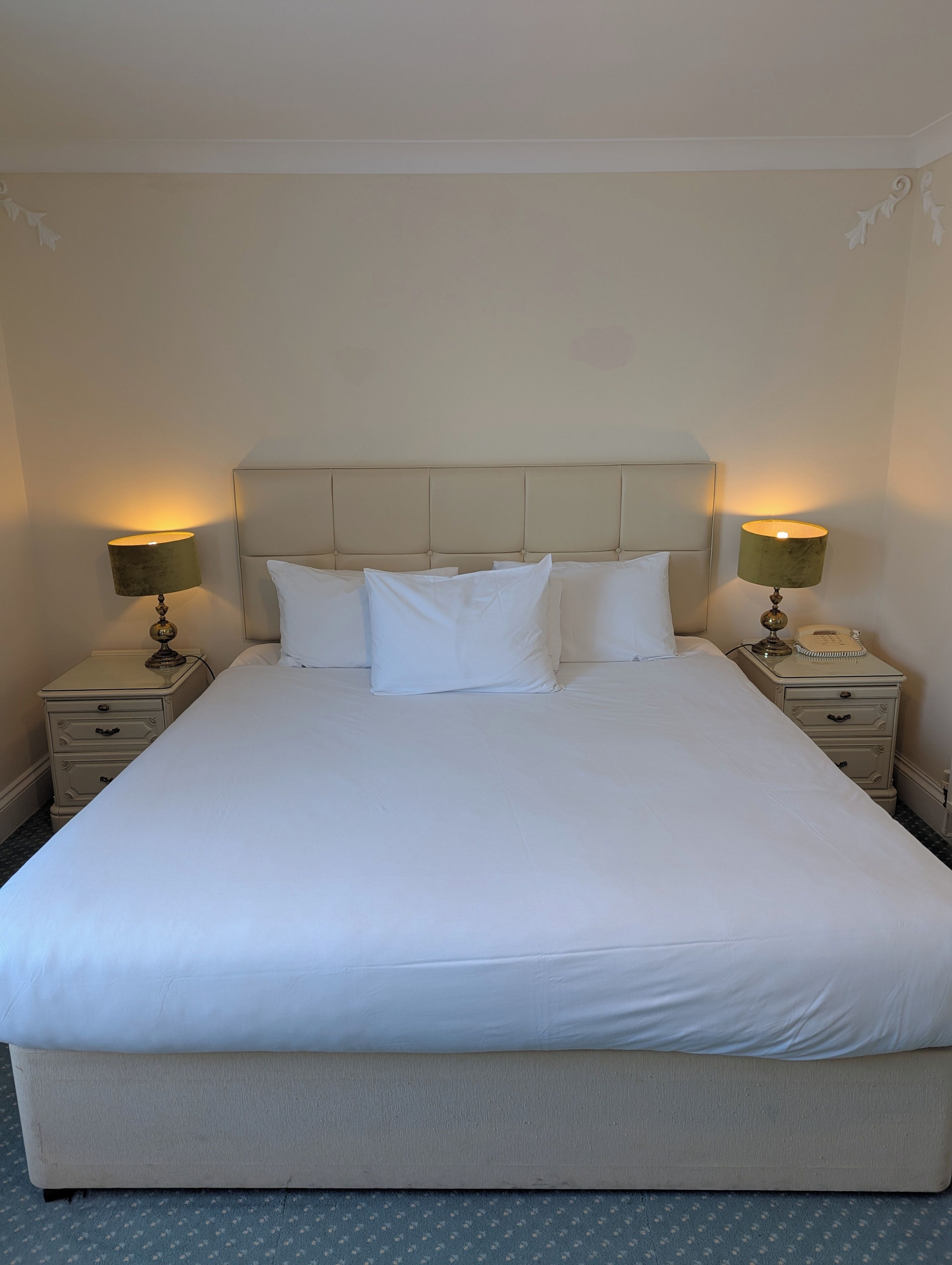 A neatly made bed with a headboard, two bedside tables with lamps, and a telephone on one of the tables.
